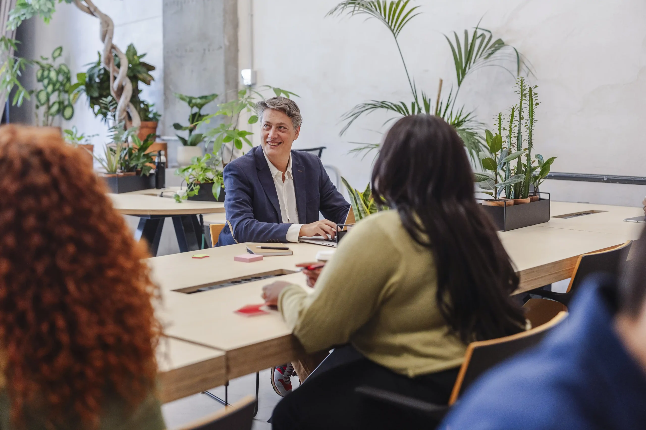 Een zakelijk gesprek aan een vergadertafel in een lichte ruimte met planten.
