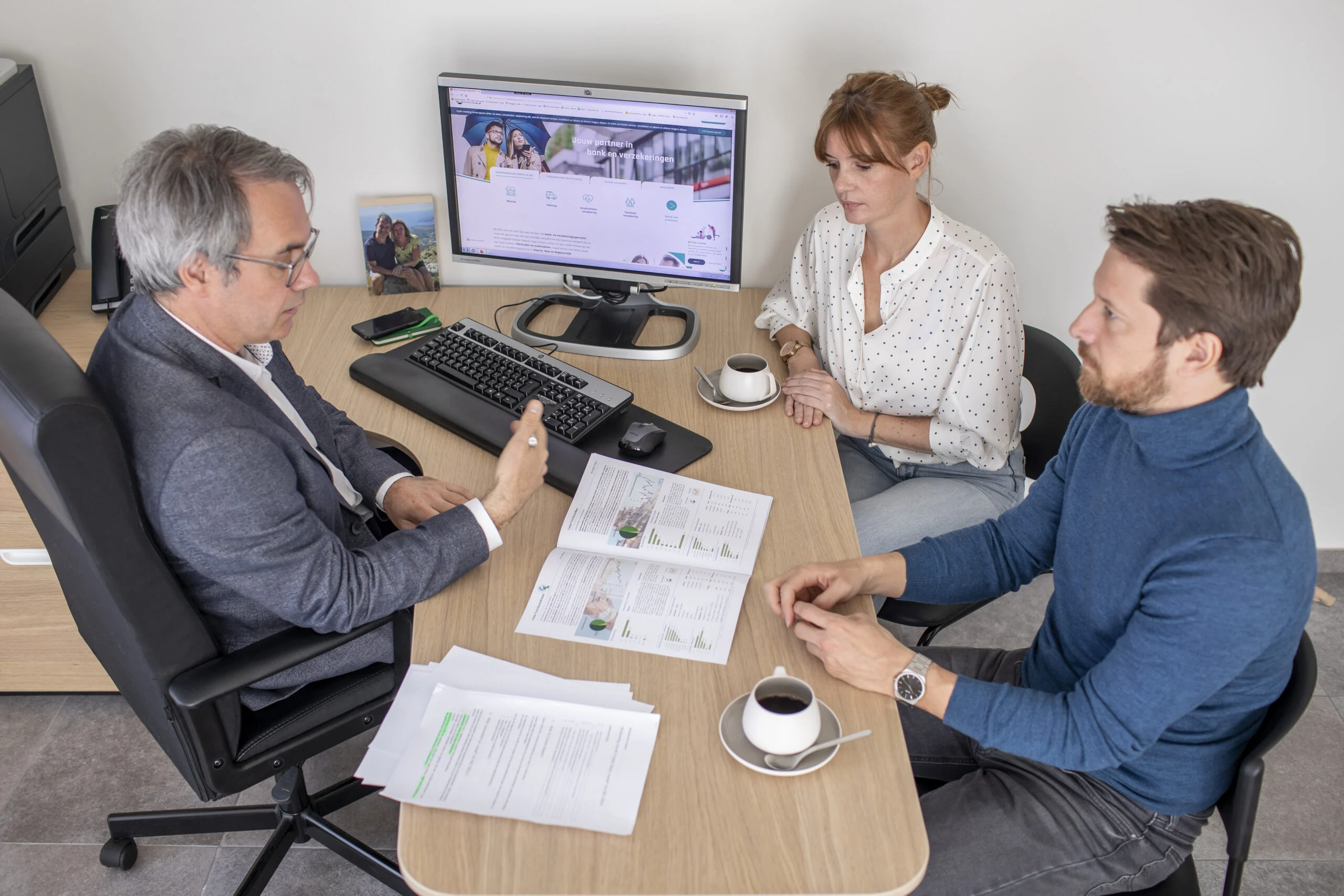 Drie collega's overleggen aan een bureau met een computerscherm.