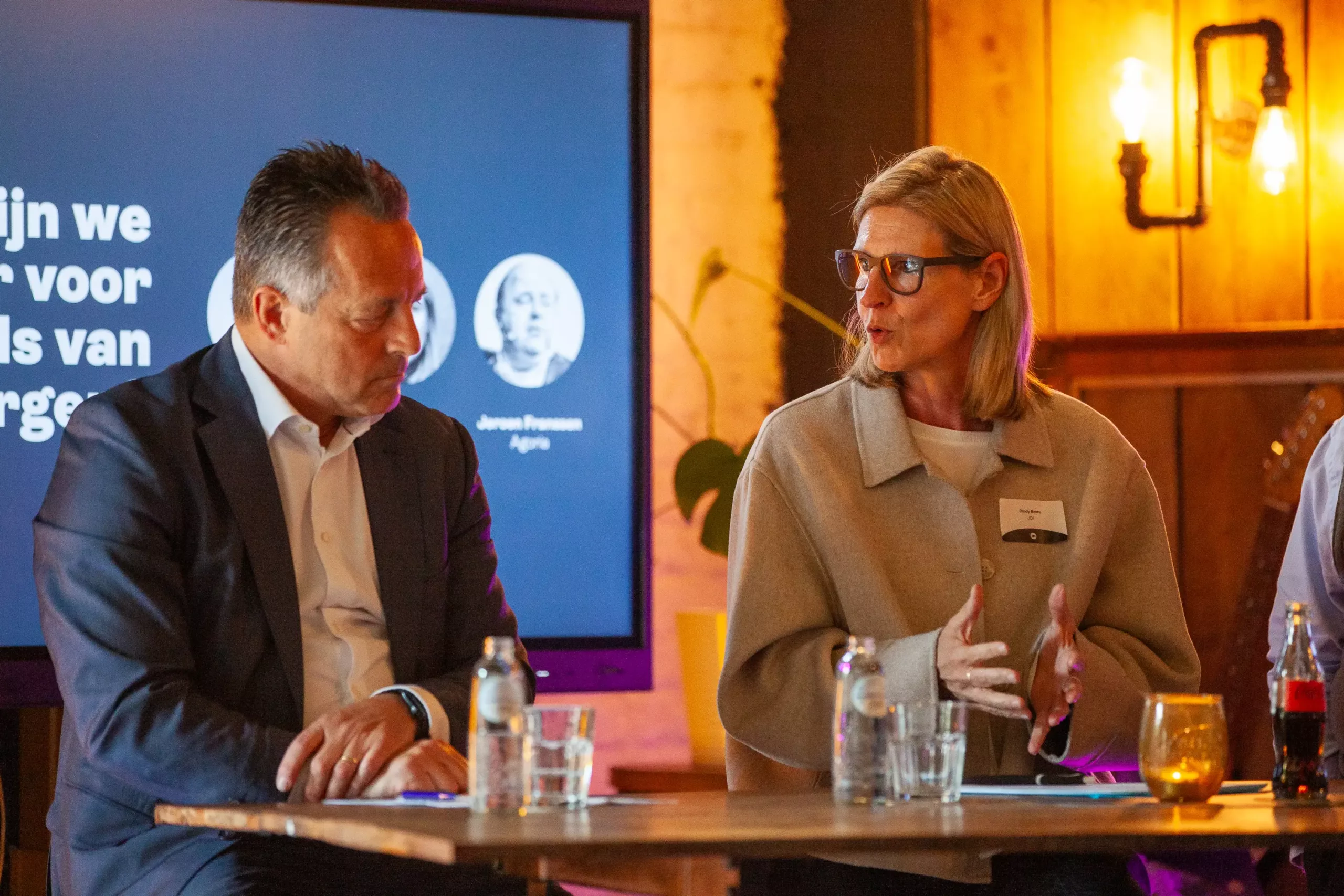 Twee mensen in gesprek aan een tafel tijdens een event van JDI.