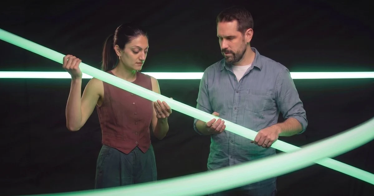 Twee collega’s houden samen een lichtgevende groene buis strak