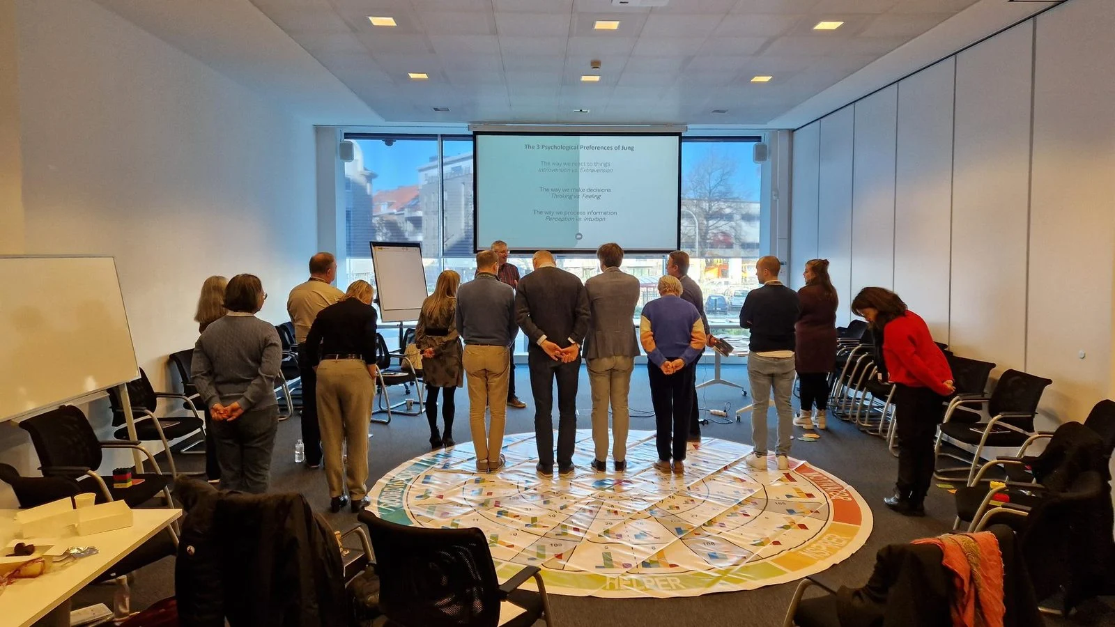 Het auditteam van Crelan staat in een kring op een mat met gekleurde ringen tijdens een Insights Discovery-workshop.