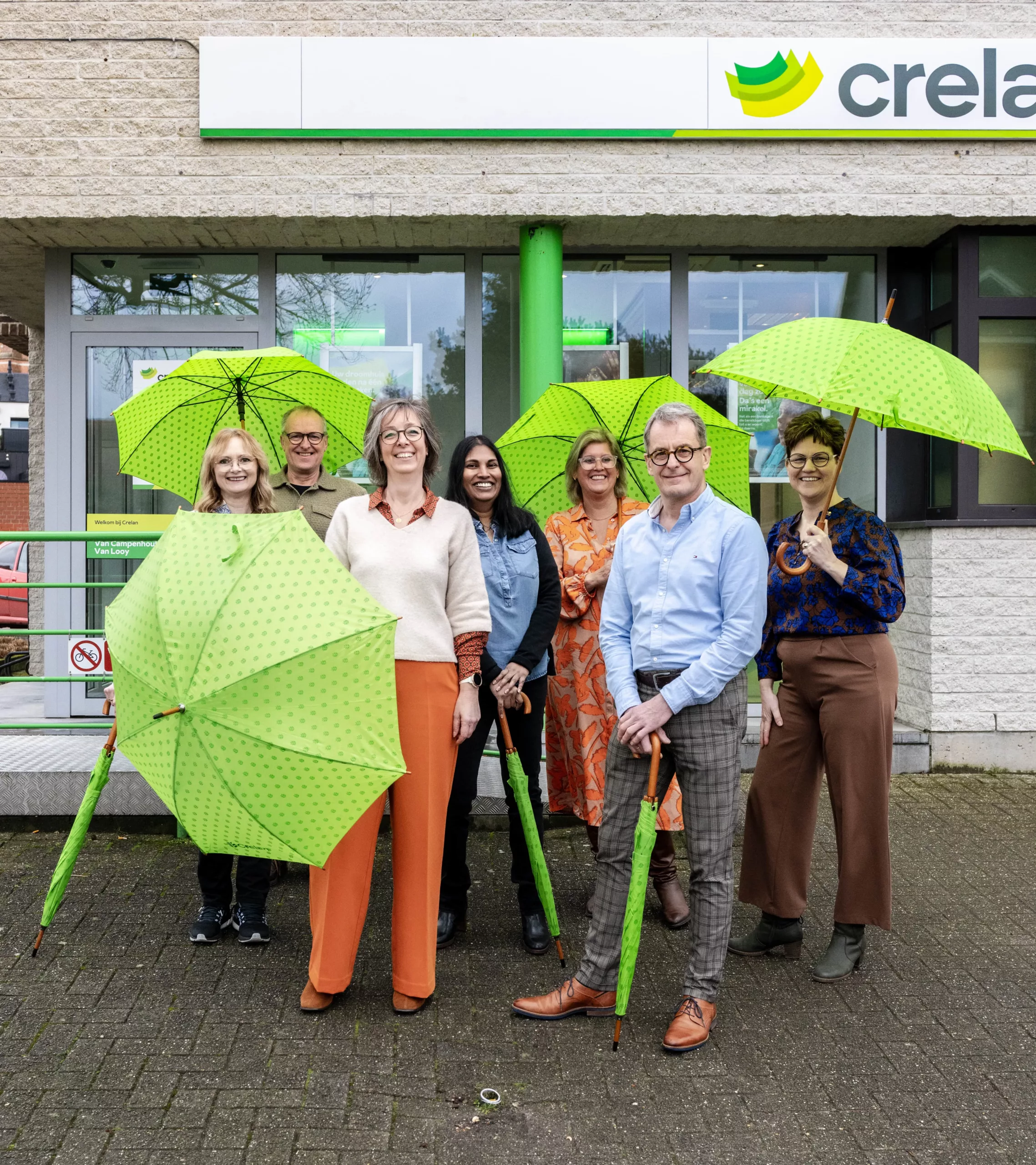 Het team van Van Campenhout-Van Looy met groene Crelan-paraplu's voor het kantoor.